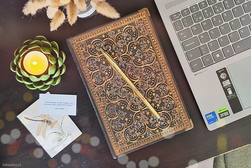 Flatlay com caderno vintage dark academia, caneta dourada, vela tealight acesa, flores secas e computador portátil aberto — ferramentas para organizar pensamentos e estimular a criatividade