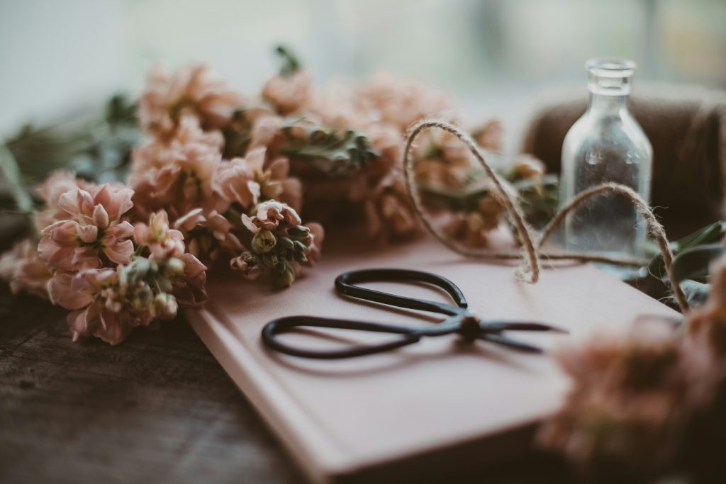 Detalhe de uma tesoura vintage rodeada de flores frescas sobre uma mesa, evocando uma rotina criativa e inspiradora