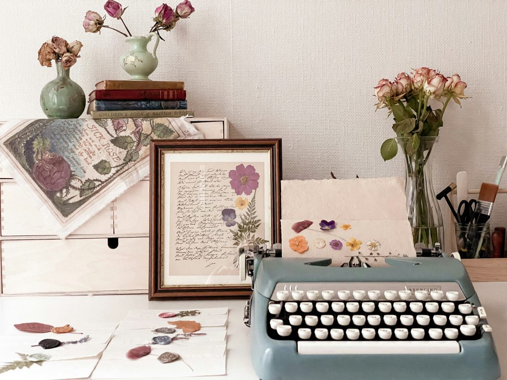 Secretária vintage com máquina de escrever antiga, livros empilhados e flores prensadas — ambiente cottagecore primaveril para trabalho criativo