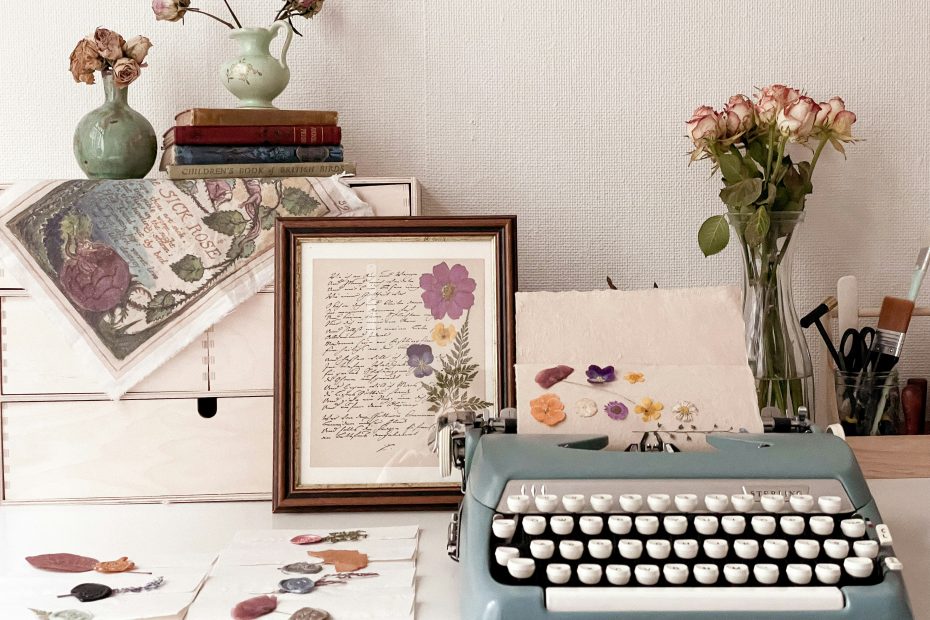 Secretária vintage com máquina de escrever antiga, livros empilhados e flores prensadas — ambiente cottagecore primaveril para trabalho criativo